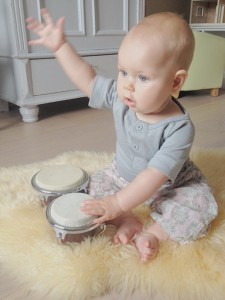 baby alma på 6 mdr. sidder på gulvet og trommer på sin baby bongo